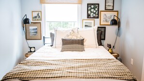 A neatly made bed with a checkered bedspread, a decorative pillow, and a bedside lamp. There are framed pictures on the wall and a small table with a clock and a vase. - JULY DISCOUNT! Romantic 2 BR 2 story w/mountain views and stunning outdoor space (Amherst)