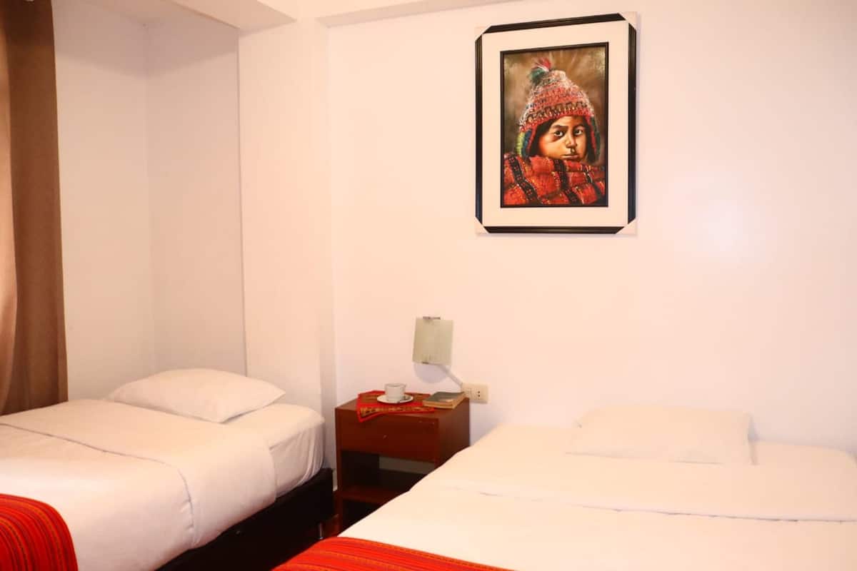 A hotel room with two single beds, a nightstand with a lamp, and a framed picture on the wall.