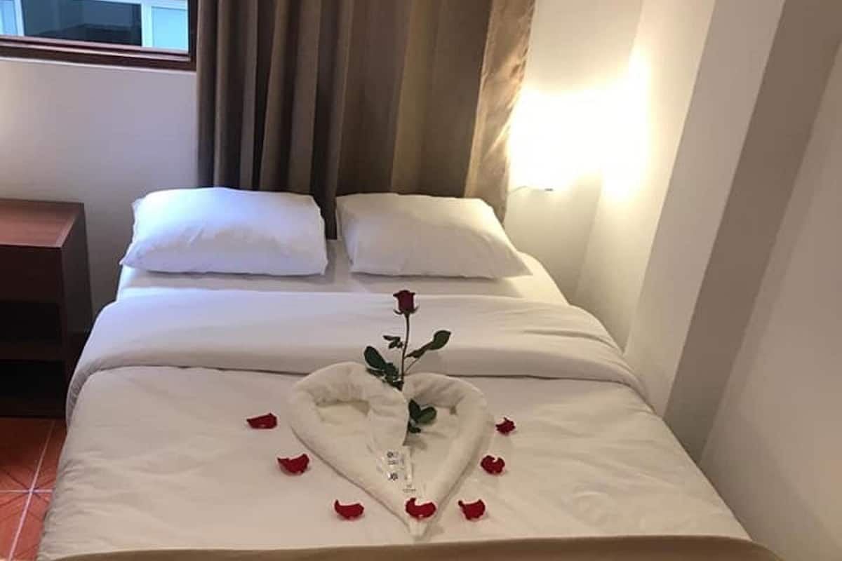 A hotel room with a bed, a nightstand, and a window with curtains.