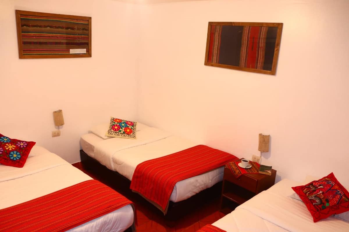 A hotel room with three beds, each with a red blanket and a colorful pillow. There are two wall-mounted artworks above the beds.