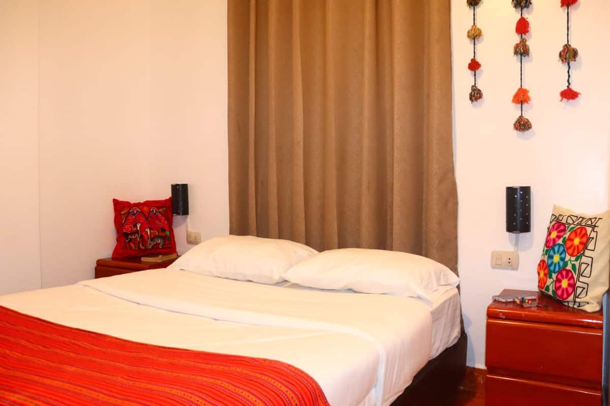 A hotel room with a bed, a nightstand, a red suitcase, and a wall with a decorative item.