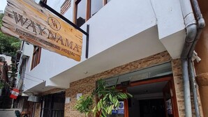 A hotel entrance with a wooden signboard, potted plants, and a tiled pavement. - Waynama Hostal (Machu Picchu)
