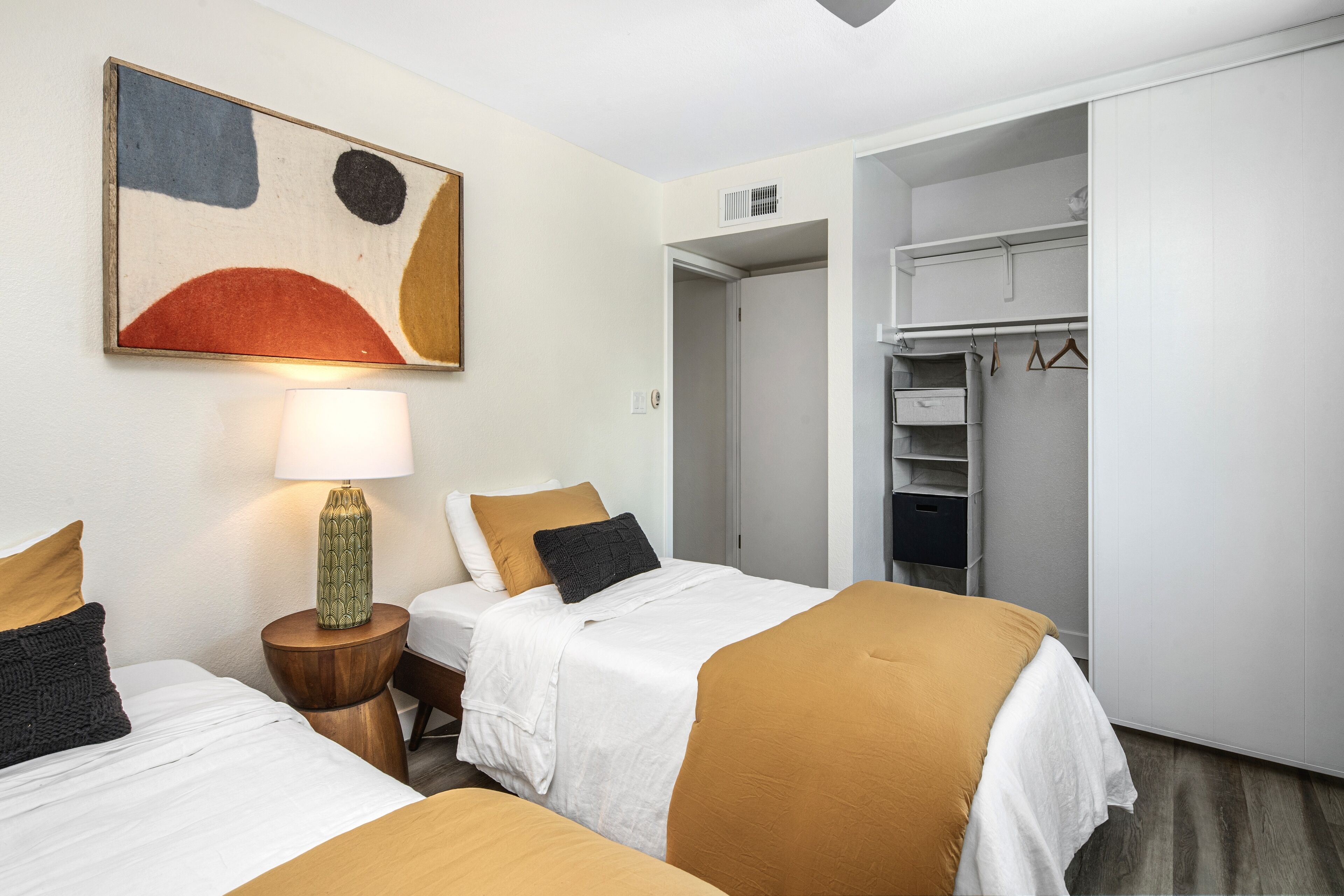 A hotel room with two beds, a wardrobe, and a painting on the wall.