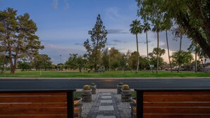 A paved pathway leading to a wooden bench area with planters, surrounded by trees and a clear sky.
