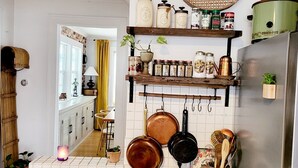 A kitchen with a stove, pots, a refrigerator, and shelves with jars and spices. - Vintage Charm — 5-Min Walk to Downtown & Campus (Eugene)