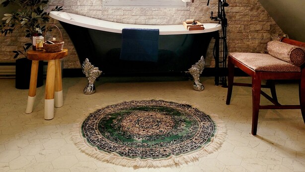 A bathroom with a freestanding bathtub, a wooden chair, a patterned rug, and a stone wall. - Vintage Charm — 5-Min Walk to Downtown & Campus (Eugene)