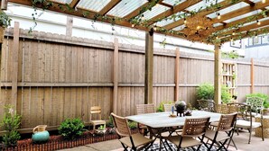 An outdoor patio area with a wooden pergola, a table with chairs, and various potted plants. - Vintage Charm — 5-Min Walk to Downtown & Campus (Eugene)