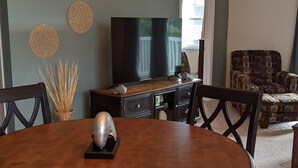 A dining area with a round table, chairs, a chandelier, a television, and decorative wall art. - 2 BR condo-pool, remote work, golf courses, and family attractions nearby (Myrtle Beach)