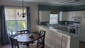 A modern kitchen with white cabinetry, a central island, and a dining area with a round table and chairs. - 2 BR condo-pool, remote work, golf courses, and family attractions nearby (Myrtle Beach)