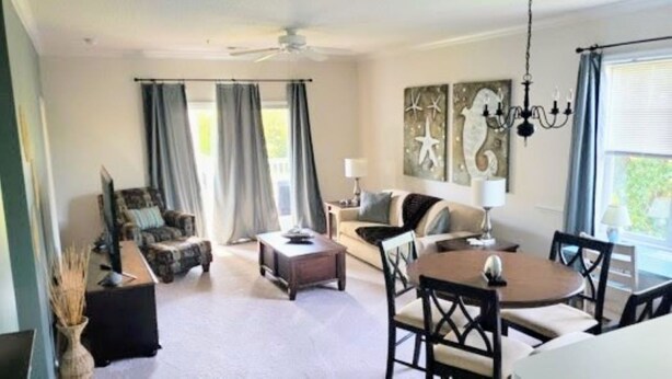 A spacious living room with a sofa, coffee table, and dining table. There is a ceiling fan, curtains, and artwork on the wall. - 2 BR condo-pool, remote work, golf courses, and family attractions nearby (Myrtle Beach)