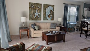 A living room with a beige sofa, two side tables with lamps, a coffee table, and a patterned rug. - 2 BR condo-pool, remote work, golf courses, and family attractions nearby (Myrtle Beach)