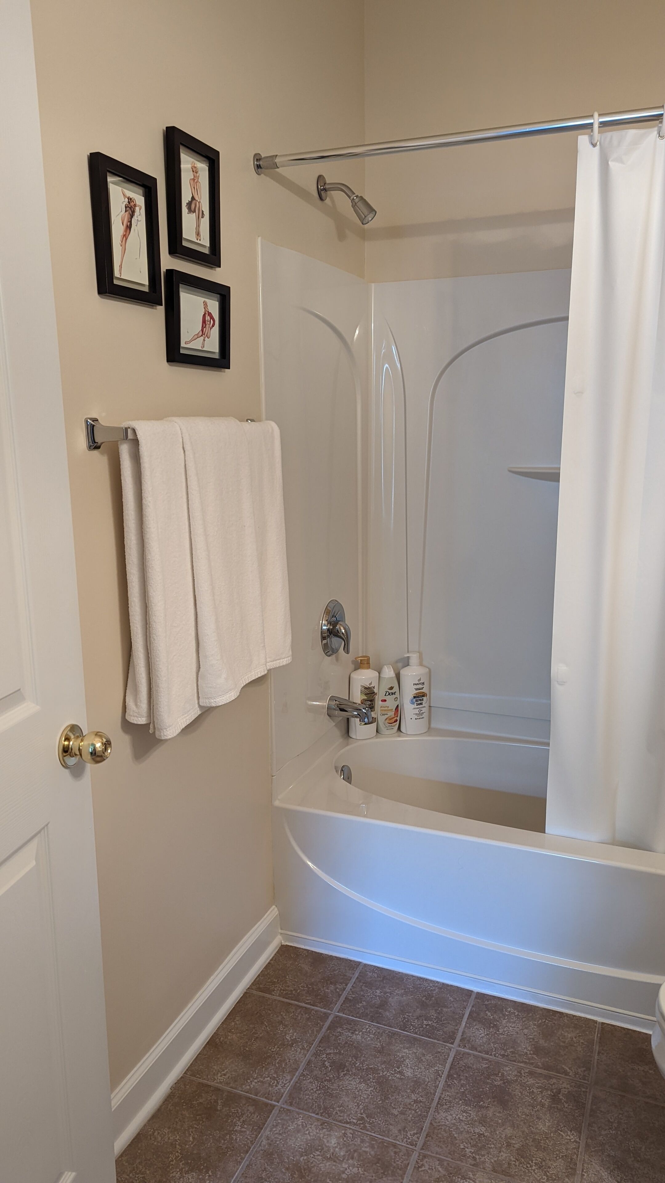 A bathroom with a bathtub, a shower curtain, and two framed pictures on the wall.
