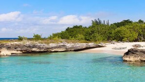 Une plage bordée d’une eau turquoise et limpide, un promontoire rocheux et, en arrière-plan, une végétation luxuriante.