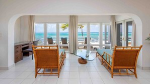 Une pièce dotée d’une grande fenêtre donnant sur la mer, meublée de chaises en osier et d’une table en verre.