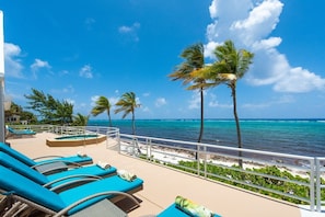 A resort pool area with lounge chairs, palm trees, and a view of the ocean. - So Serene Oceanfront Villa, Rum Point, Private Beach, Hot Tub, Kayak, Snorkeling (Grand Cayman)