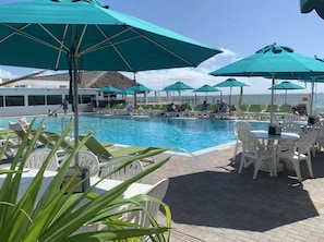 Een zwembadterras met ligbedden en parasols, een zwembad en uitzicht op de oceaan.