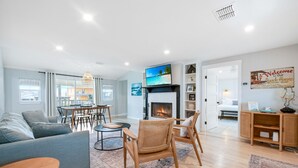 Uma sala de estar moderna com lareira, sofá, espaço de refeições e vista para a praia.