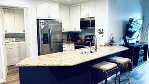 A modern kitchen with white cabinets, stainless steel appliances, a granite countertop, and a bar area with stools.