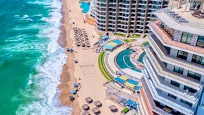 A coastal hotel with a beachfront, a pool, and multiple balconies.