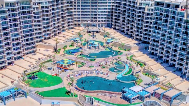 A high-rise hotel with multiple balconies, a central pool area, and a beachside location.