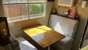 A compact kitchenette with a small table and bench, a window with blinds, and an air conditioning unit. - Get off the grid in south La (Bayou Vista)