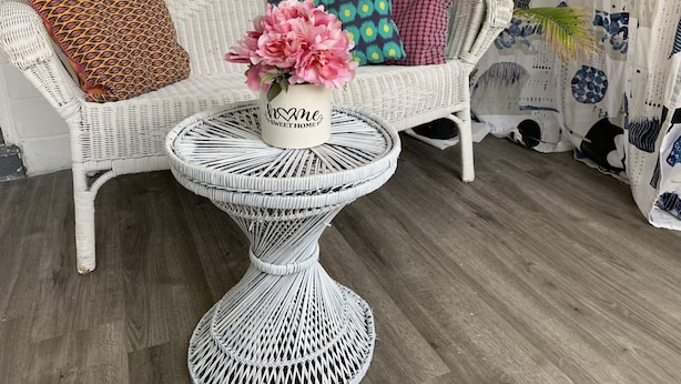 A wicker sofa with patterned cushions, a small round table with a floral centerpiece, and a potted plant.