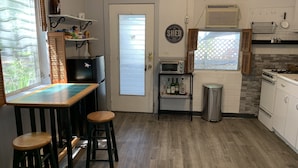 A kitchen with a wooden countertop, stools, a refrigerator, a microwave, a stove, and a window with blinds.