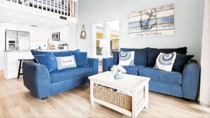 En moderne stue med to blå sofaer, et hvidt sofabord og et køkken i baggrunden.