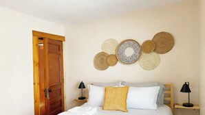 A bedroom with a bed, bedside tables, a wooden door, and wall decorations.
