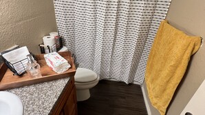 Un baño con inodoro blanco, tocador de madera, encimera de granito, toallero con toalla amarilla y cortina de ducha estampada en blanco y negro.