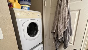 Un área de lavandería con lavadora y secadora apiladas, una botella de detergente y toallas colgadas en la puerta.