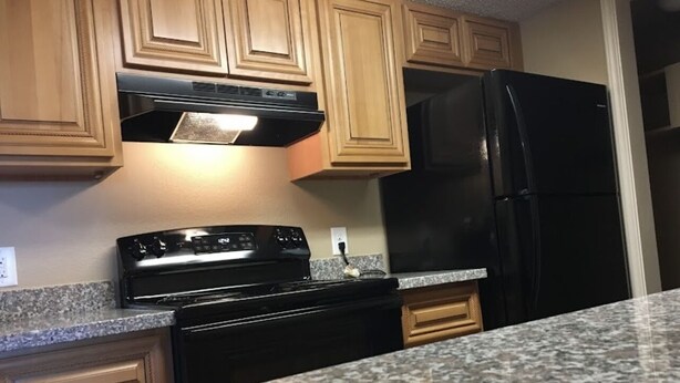 Una cocina con armarios de madera, una estufa negra y un refrigerador negro.