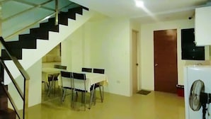 A spacious living area with a staircase, a dining table set with chairs, a television, and a refrigerator. - 2020 Travelers Inn (Dumaguete)