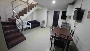 A modern interior with a staircase, a dining area, a sofa, and a TV mounted on the wall. - 2020 Travelers Inn (Dumaguete)