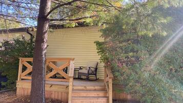Une terrasse en bois avec un escalier menant à une zone abritée, entourée d’arbres et d’une maison.