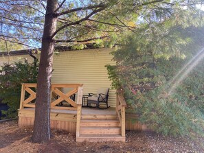 A wooden deck with a staircase leading to a covered area, surrounded by trees and a house.