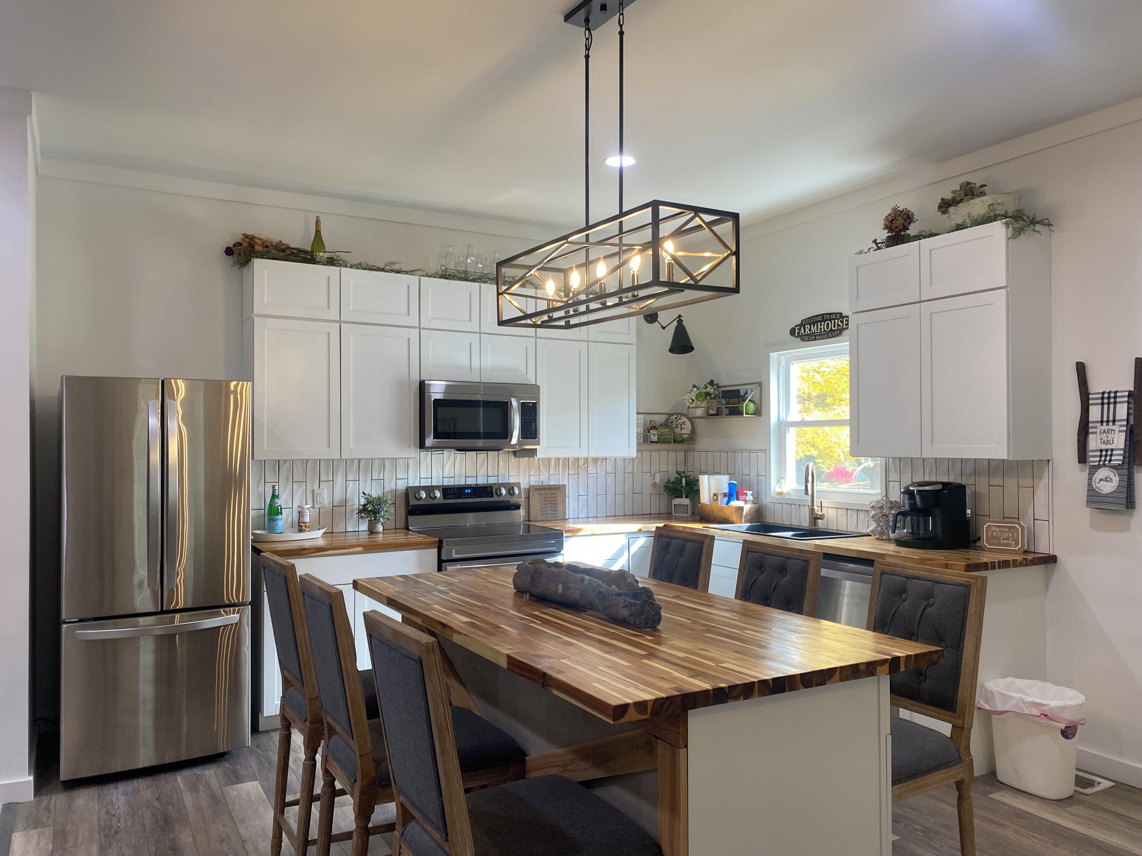 A modern kitchen with stainless steel appliances, a wooden dining table, and a farmhouse sign.