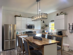 A modern kitchen with stainless steel appliances, a wooden dining table, and a farmhouse sign.