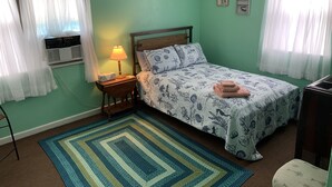 A room with a bed, a nightstand with a lamp, a window with curtains, and a wall with two framed pictures. - Beach Side Studio #5 -  Pet Friendly, WiFi, Off-Street Parking, Large Smart TV (Norfolk)