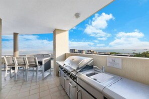 Un balcon avec un barbecue et des chaises, offrant une vue sur le paysage urbain et l’étendue d’eau.