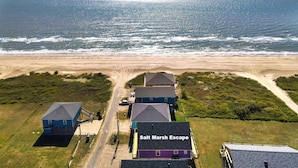Vista aérea de uma propriedade costeira chamada "Salt Marsh Escape", com uma praia, oceano e algumas casas.