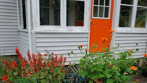 Een huis met een witte gevel en een oranje deur, omgeven door een tuin met diverse bloemen en planten.