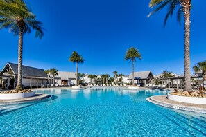 Une piscine d’eau cristalline, entourée de palmiers et de bâtiments de style hôtelier, avec des chaises longues.