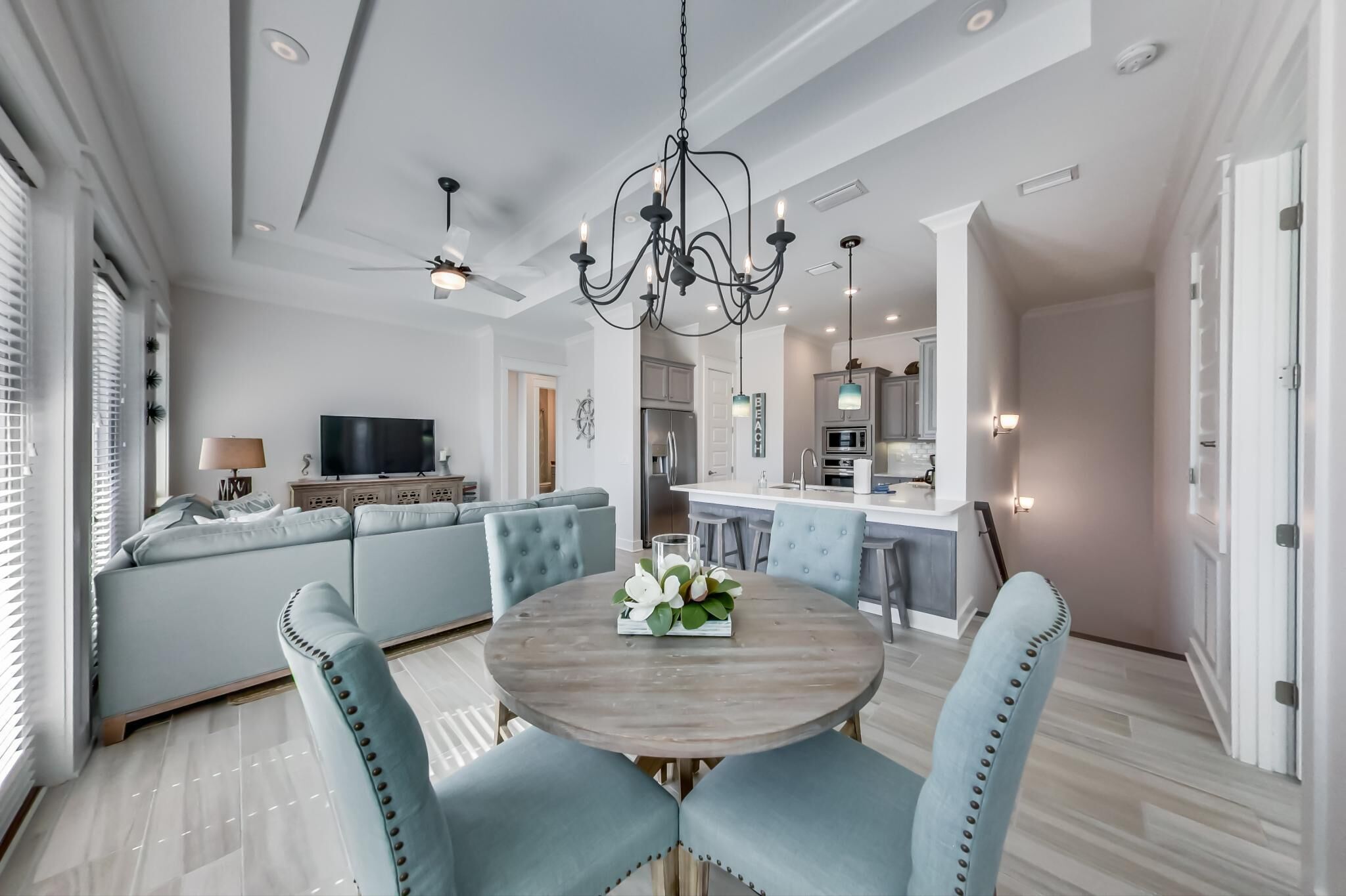 En moderne stue med sofa, spisebord med stole, en lysekrone og et køkken i baggrunden.
