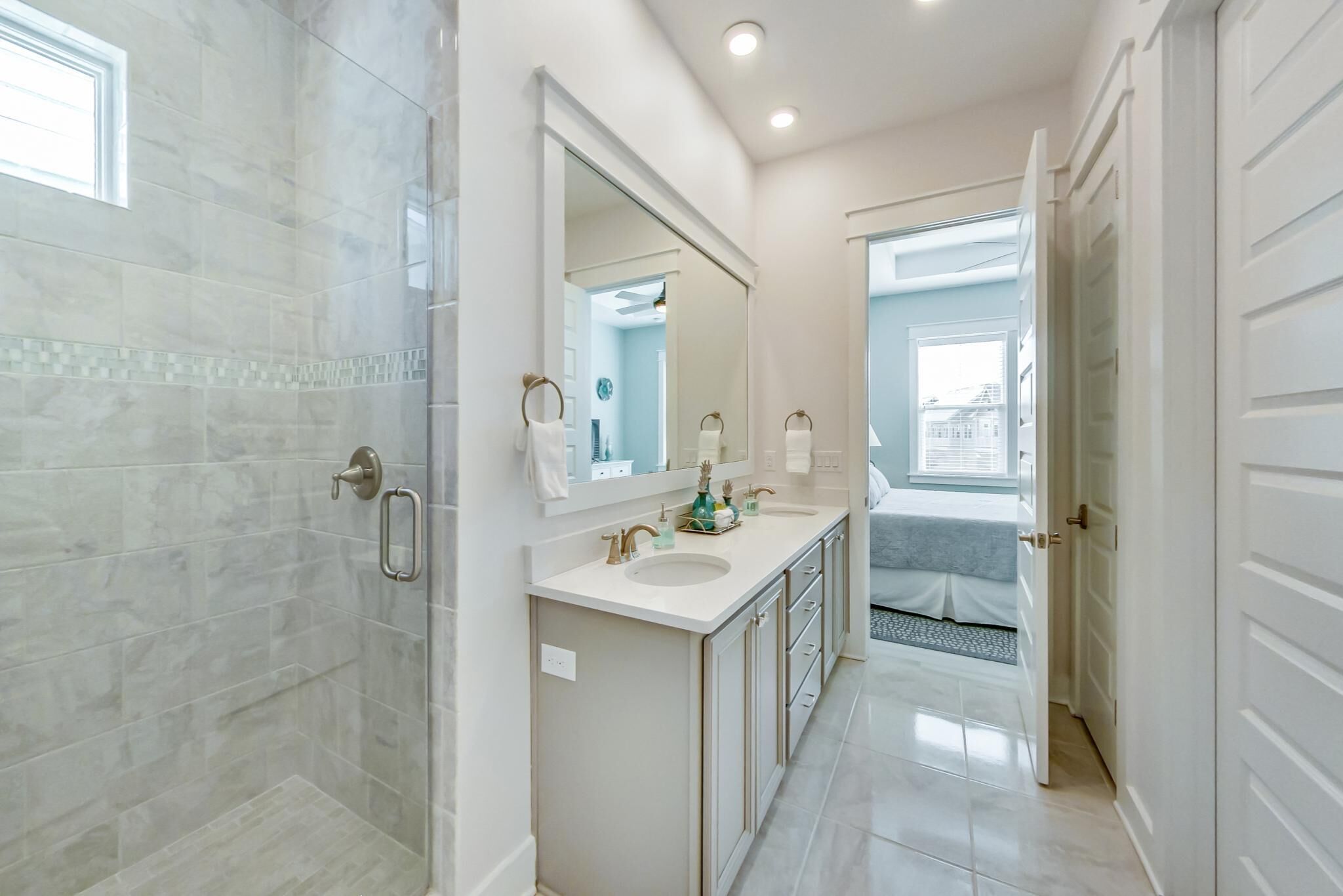 Un baño moderno con cabina de ducha de vidrio, un espejo grande y un tocador con lavamanos y armario.