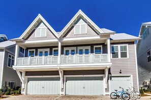 Une maison à deux étages avec un balcon, deux garages et un vélo garé à l’extérieur.