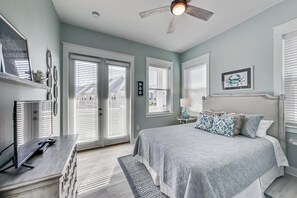 Une chambre à coucher avec un lit, un bureau, un ventilateur de plafond et de grandes fenêtres.