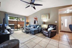 A spacious living room with a ceiling fan, a sliding glass door leading to an outdoor area, a fireplace, and a comfortable seating arrangement. - Cozy Cottage,  private back yard, and free coffee! (Wildwood)