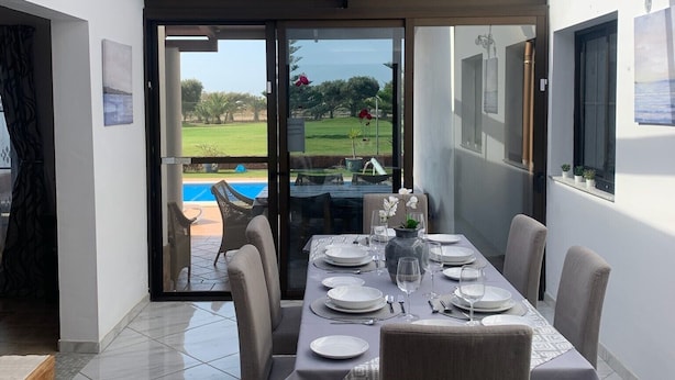 Comedor con una mesa dispuesta para seis, puerta de vidrio que da a una piscina y vistas al exterior.