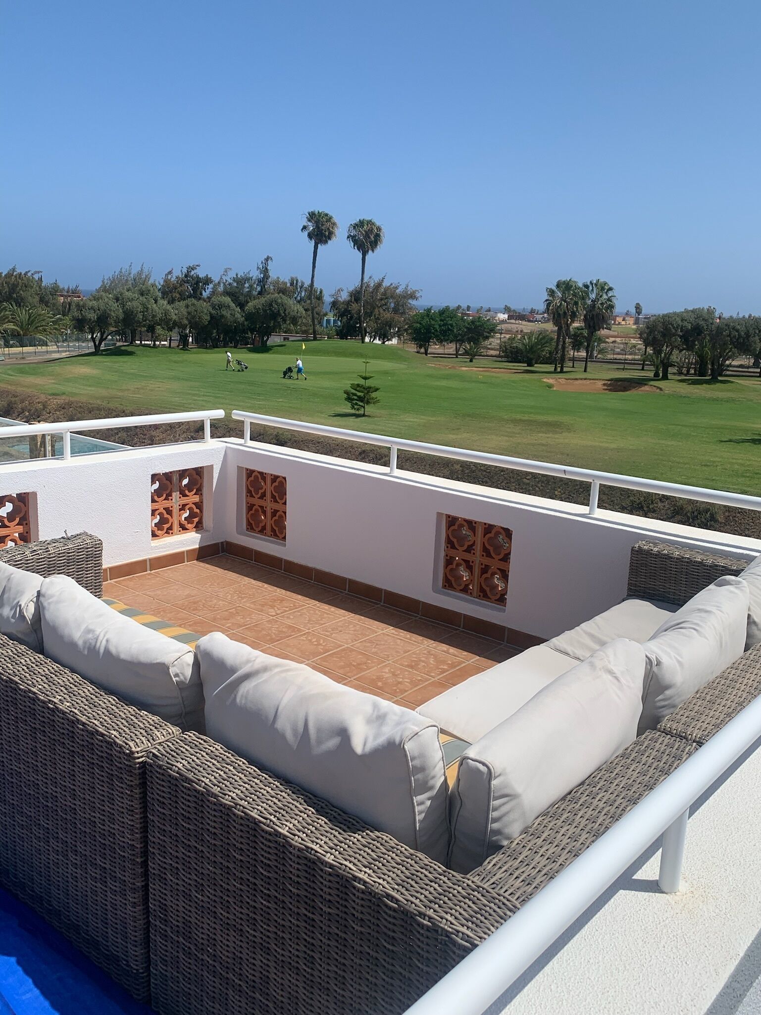 Terraza en la azotea con mobiliario de mimbre y vistas a un campo de golf.